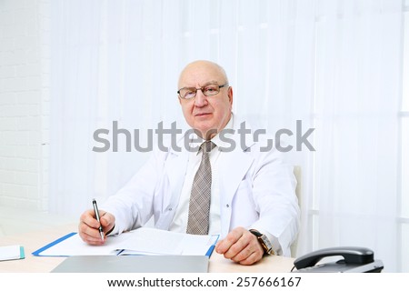 Portrait of professional doctor at table in his office on white curtain background