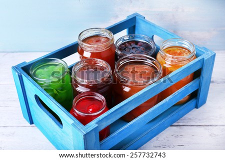 Homemade jars of fruits jam in crate on wooden table and color wall background