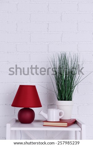 Interior design with lamp, plant, ceramic watering pot and book on tabletop on white brick wall background