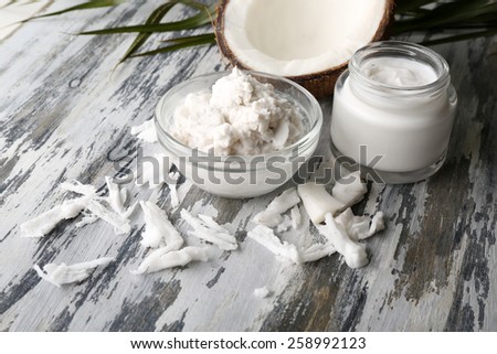 Coconut with coconut oil in bowl with jar of cosmetic cream on wooden background