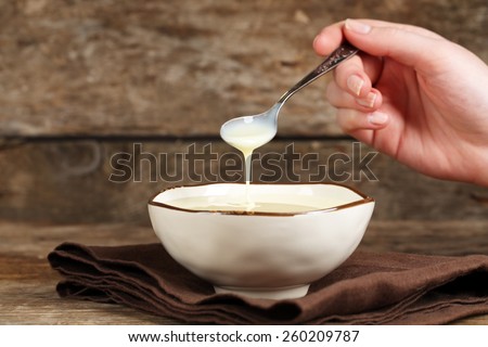 Bowl with condensed milk and spoon on napkin on wooden background