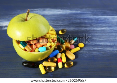Apple and colorful pills, on color wooden background