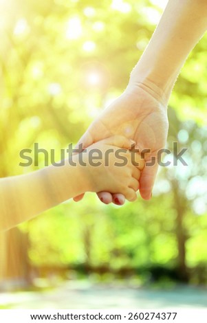 Mom and daughter hands on sunny nature background