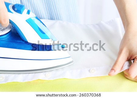 Woman ironing shirt on ironing board in room