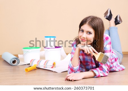 Beautiful girl lying on floor with equipment for painting wall