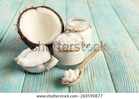 Fresh coconut oil in glassware and wooden spoon on color wooden table background