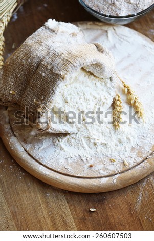 Flour in burlap bag on cutting board and wooden table background