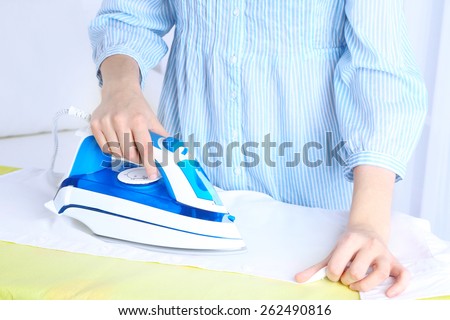 Woman ironing shirt on ironing board in room