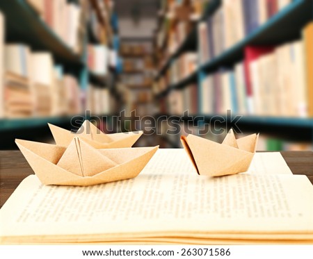 Open book with paper ships on bookshelves background