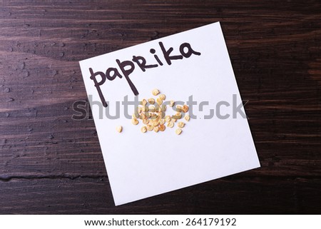 Paprika seeds on piece of paper on wooden background