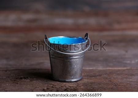Metal bucket with colorful paint on wooden background
