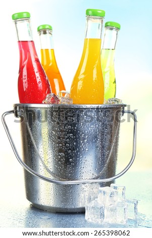 Bottles of tasty drink in metal bucket with ice on bright background