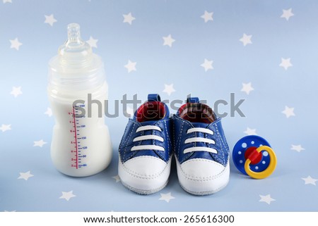 Baby shoes with nipple and bottle of milk on blue background
