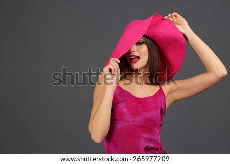 Beautiful young woman in pink dress and hat on dark gray background