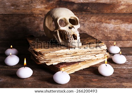 Still life with human skull, retro book and candlelight on wooden table, closeup