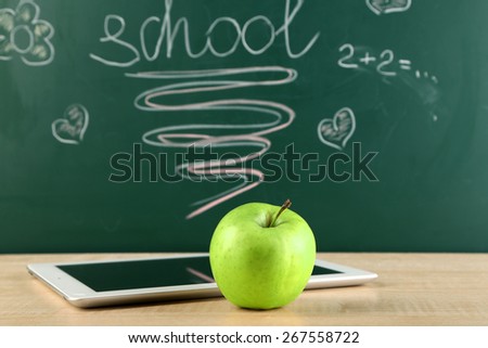 Digital tablet and apple on  desk in front of blackboard