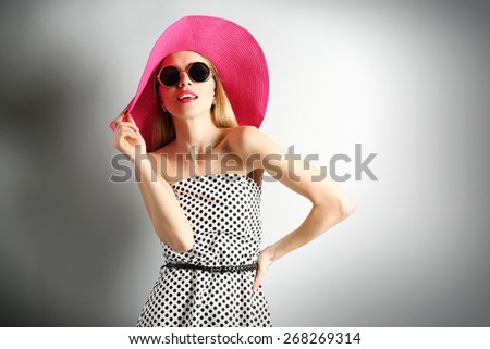 Expressive young model in pink hat with sunglasses on gray background