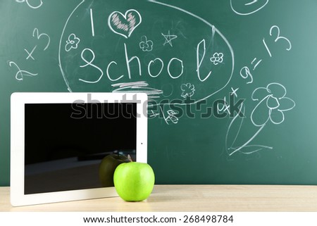 Digital tablet and apple on  desk in front of blackboard