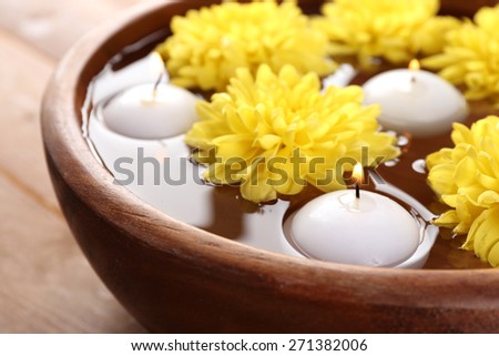 Bowl of spa water with flowers and candles on wooden table, closeup