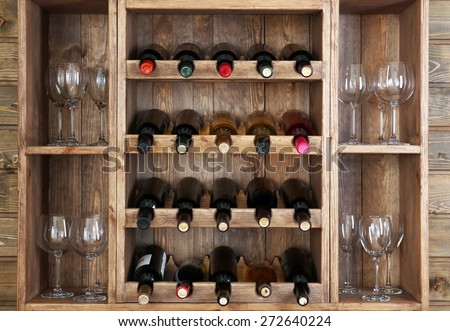 Shelving with wine bottles and glasses on wooden wall background