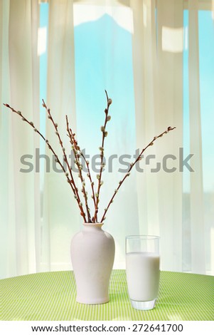 Willow twigs and glass of milk on table on curtains background