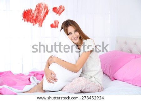 Beautiful young woman dreaming about love and sitting on bed