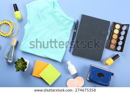 Female shirt, cosmetics and office details on color table, top view