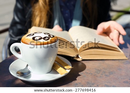 Woman reading book and cup of cappuccino in cafe, outdoors