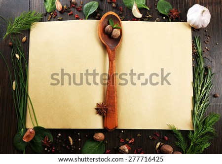 Open recipe book with fresh herbs and spices on wooden background