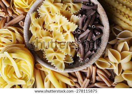 Different types of pasta with wooden bowl, macro view