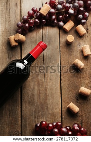 Glass bottle of wine with corks and grapes on wooden table background