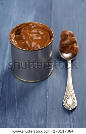 Can of boiled condensed milk with spoon on color wooden table background