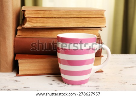 Books and cup on wooden table, on curtains background