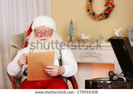Santa Claus sitting with list of children wishes in comfortable chair near fireplace at home
