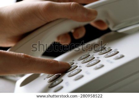 Finger pressing number button on telephone to make a call, close up