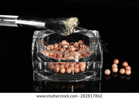 Jar with cosmetic powder balls and makeup brush, isolated on black