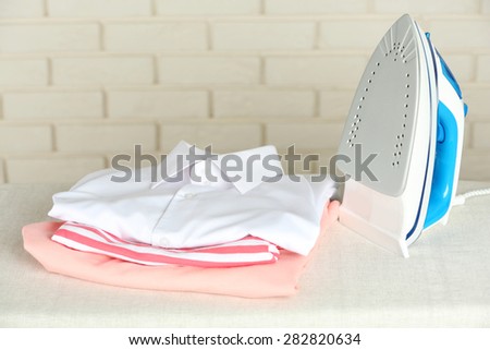 Pile of clothes and electric iron on brick wall background