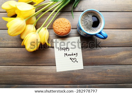 Cup of coffee with fresh cupcake, tulips and Happy Monday massage on wooden background