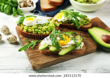 Tasty sandwiches with egg, avocado and vegetables on wooden background