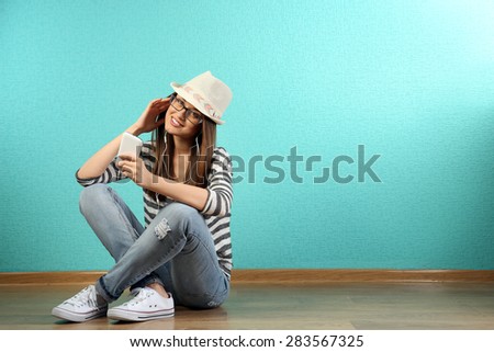 Young woman sitting on floor with headphones on turquoise wallpaper background