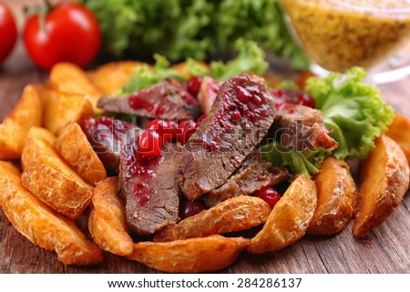 Beef with cranberry sauce, roasted potato slices and bun on wooden cutting board, close-up
