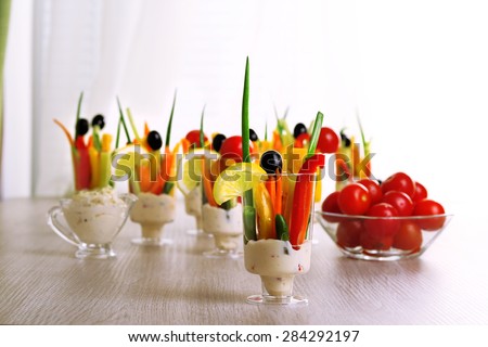 Snack of vegetables in glassware on wooden table, on curtains background