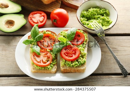 Vegan sandwich with avocado and vegetables on plate, on wooden background