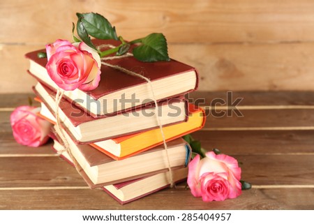 Tied books with pink roses on wooden background