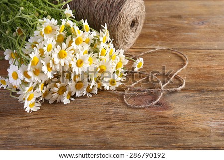 Beautiful bouquet of daisies with twine on wooden background
