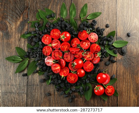 Cherry tomatoes with raisins arranged in heart shape on wooden background