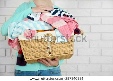 Woman holding basket with heap of different clothes, on bricks wall background