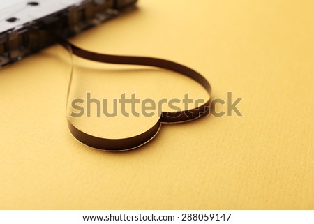 Audio cassette with magnetic tape in shape of heart on yellow background