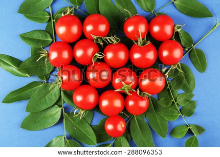 Cherry tomatoes arranged in heart shape with green leaves on blue background