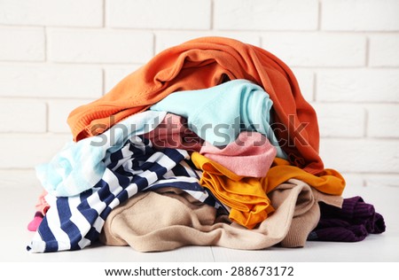 Heap of different clothes on wooden table, on bricks wall background